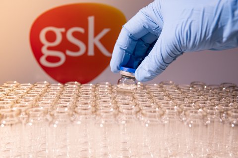 GSK name in blur. Vaccine scientist holding the glass vial with vaccine.