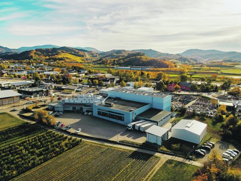 Luftaufnahme eines Industrieareals mit Produktionsgebäuden, Lkw-Andockstationen und umliegenden Feldern.